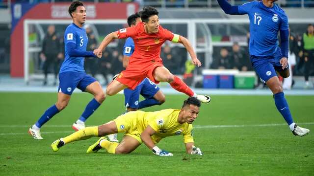 Aksi bintang Timnas China, Wu Lei (merah) saat menghadapi hadangan dari kiper Timnas Singapura, Hassan Sunny di putaran kedua Kualifikasi Piala Dunia 2026. (AFP).