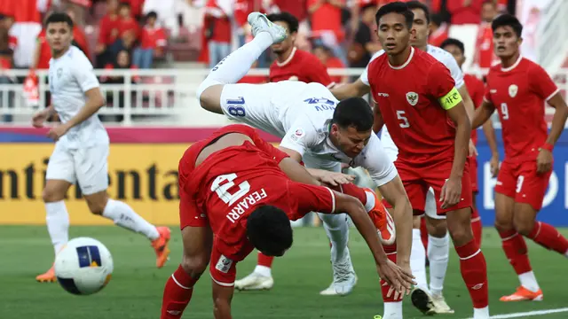 Pemain Timnas Indonesia U-23, Muhammad Ferarri (kiri) dan pemain Uzbekistan U-23, Alibek Davronov terjatuh dalam perebutan bola pada laga semifinal Piala Asia U-23 2024 di Abdullah bin Khalifa Stadium, Doha, Qatar, Senin (29/4/2024). (AFP/Karim Jaafar)