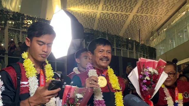 Pelatih Timnas Indonesia U-22 Indra Sjafri (kanan) memamerkan medali emas SEA Games 2023 saat tiba di Bandara Soekarno Hatta, Tangerang, Banten pada Kamis (18/5/2023) malam WIB. Garuda Nusantara sukses mengakhiri paceklik emas cabor sepak bola SEA Games usai mengalahkan Thailand di babak final. (Liputan6.com/Melinda Indrasari)