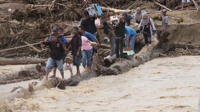 Inisiatif membuat jembatan darurat dari kayu gelondongan ini merupakan upaya relawan dan masyarakat setempat agar aktivitas dan penyaluran bantuan dapat dilakukan. Tampak dalam foto, warga yang menjadi korban banjir menggunakan kayu gelondongan untuk menyeberangi sungai di Batang Toru, Sumatra Utara, Selasa 2 Desember 2025. (AP Photo/Binsar Bakkara)